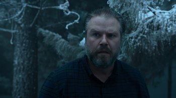 Movie still from “Escape Room” (2019), directed by Adam Robitel – A man with a goatee and beard in a forest; Close Up shot, Low angle