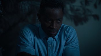 Movie still from “Escape Room” (2019), directed by Adam Robitel – A man sitting in a dark room wearing a blue shirt; Close Up shot, Low angle