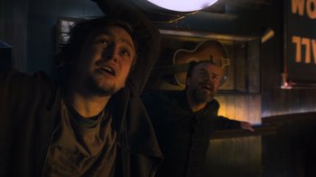 Movie still from “Escape Room” (2019), directed by Adam Robitel – Two men are standing in a room with a guitar in front of them; Medium shot, Low angle