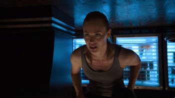 Movie still from “Escape Room” (2019), directed by Adam Robitel – A woman in grey tank top standing in a dark room; Medium shot, Low angle