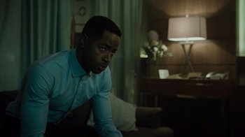 Movie still from “Escape Room” (2019), directed by Adam Robitel – A man sitting on a couch in a living room; Medium shot, Over the shoulder angle