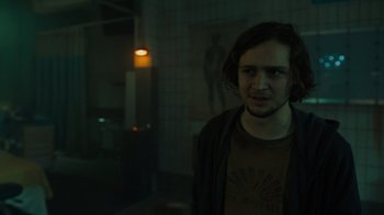 Movie still from “Escape Room” (2019), directed by Adam Robitel – A man standing in a dark room in front of a painting; Medium shot, Over the shoulder angle