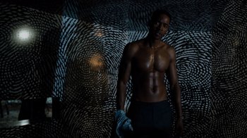 Movie still from “Escape Room” (2019), directed by Adam Robitel – A man standing in front of a wall covered in fingerprint patterns; Medium shot, Overhead angle