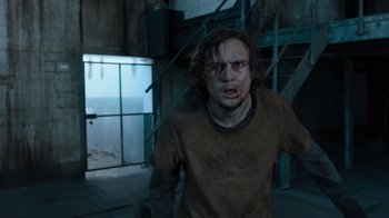 Movie still from “Escape Room” (2019), directed by Adam Robitel – A man in a brown t - shirt is in an abandoned building; Medium shot, Over the shoulder angle