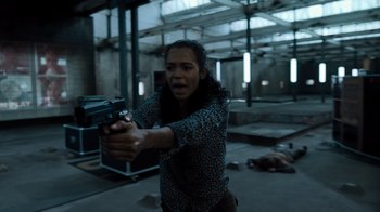 Movie still from “Escape Room” (2019), directed by Adam Robitel – A woman holding a gun in a room with other people; Medium shot, Over the shoulder angle