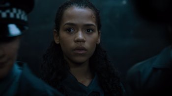 Movie still from “Escape Room” (2019), directed by Adam Robitel – A young woman with long black curly hair looking at the camera; Close Up shot, Low angle
