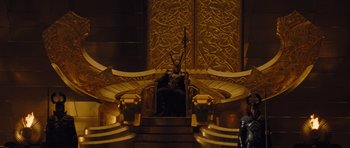 Movie still from “Thor” (2011), directed by Kenneth Branagh – A statue sitting on top of a chair in a room; Wide shot, Low angle