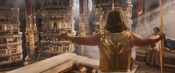 Movie still from “Thor: Love and Thunder” (2022), directed by Taika Waititi – A man in a gold vest pointing to a building; Medium shot, Low angle