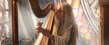 Movie still from “Thor: Love and Thunder” (2022), directed by Taika Waititi – An older man playing a harp in a church; Medium shot, Low angle