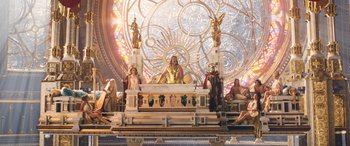 Movie still from “Thor: Love and Thunder” (2022), directed by Taika Waititi – A group of people sitting around a table with a statue; Extreme Wide shot, Low angle