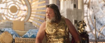 Movie still from “Thor: Love and Thunder” (2022), directed by Taika Waititi – A man in a gold outfit is standing in front of a building; Medium shot, Low angle