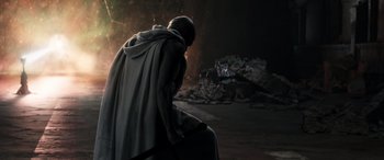 Movie still from “Thor: Love and Thunder” (2022), directed by Taika Waititi – A man wearing a cape and sitting on a chair in the dark; Wide shot, Low angle