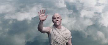 Movie still from “Thor: Love and Thunder” (2022), directed by Taika Waititi – A bald man in a toga waves at the camera; Medium shot, Low angle