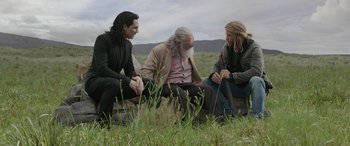 Movie still from “Thor: Ragnarok” (2017), directed by Taika Waititi – A group of men sitting on top of a grass covered field; Wide shot, Over the shoulder angle