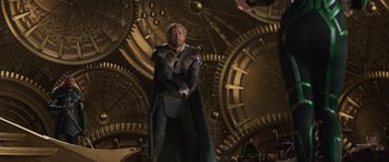 Movie still from “Thor: Ragnarok” (2017), directed by Taika Waititi – A man dressed as thor standing in front of a wall of gears; Medium shot, Over the shoulder angle