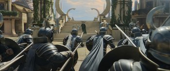 Movie still from “Thor: Ragnarok” (2017), directed by Taika Waititi – A group of men in armor and helmets stand in front of a staircase; Wide shot, Over the shoulder angle