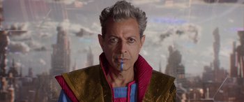 Movie still from “Thor: Ragnarok” (2017), directed by Taika Waititi – An older man wearing a red and gold jacket; Close Up shot, Over the shoulder angle