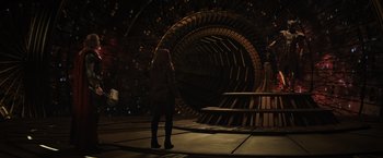 Movie still from “Thor: The Dark World” (2013), directed by Alan Taylor – A woman standing in front of a large metal object; Extreme Wide shot, Over the shoulder angle