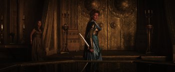 Movie still from “Thor: The Dark World” (2013), directed by Alan Taylor – A woman dressed as a knight holding a sword in front of an ornate wall; Medium shot, Over the shoulder angle