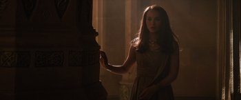 Movie still from “Thor: The Dark World” (2013), directed by Alan Taylor – A woman in a dress standing next to a pillar; Medium shot, Over the shoulder angle