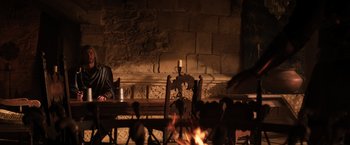 Movie still from “Thor: The Dark World” (2013), directed by Alan Taylor – A man sitting at a table in front of a fireplace; Wide shot, High angle