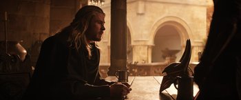 Movie still from “Thor: The Dark World” (2013), directed by Alan Taylor – A man with long blonde hair sitting at a table with a mug; Medium shot, Over the shoulder angle