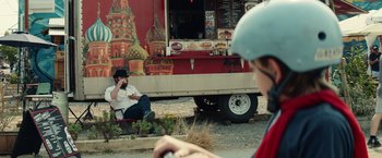 Movie still from “Timmy Failure: Mistakes Were Made” (2020), directed by Tom McCarthy – A man sitting in front of a food truck on the side of the road; Wide shot, Over the shoulder angle
