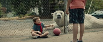 Movie still from “Timmy Failure: Mistakes Were Made” (2020), directed by Tom McCarthy – A boy sitting on the ground next to a fence with a ball; Wide shot, Over the shoulder angle