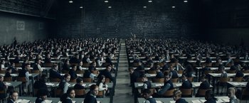 Movie still from “Timmy Failure: Mistakes Were Made” (2020), directed by Tom McCarthy – A large group of people sitting at desks in front of a brick wall; Extreme Wide shot, High angle