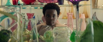 Movie still from “Timmy Failure: Mistakes Were Made” (2020), directed by Tom McCarthy – A young boy is looking at the camera in front of many glass vases; Close Up shot, Over the shoulder angle