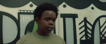 Movie still from “Timmy Failure: Mistakes Were Made” (2020), directed by Tom McCarthy – A young boy with a green shirt is standing in front of a building; Close Up shot, Low angle