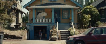 Movie still from “Timmy Failure: Mistakes Were Made” (2020), directed by Tom McCarthy – A woman standing in front of a house next to a bear; Extreme Wide shot, Low angle
