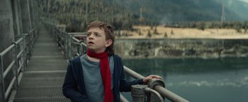 Movie still from “Timmy Failure: Mistakes Were Made” (2020), directed by Tom McCarthy – A young boy wearing a red scarf standing next to a railing; Medium shot, Low angle