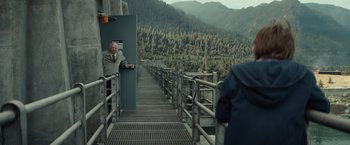 Movie still from “Timmy Failure: Mistakes Were Made” (2020), directed by Tom McCarthy – A man standing on a metal railing next to trees; Wide shot, Over the shoulder angle