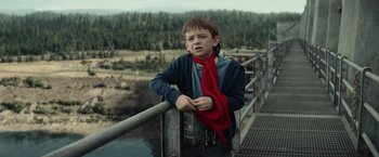 Movie still from “Timmy Failure: Mistakes Were Made” (2020), directed by Tom McCarthy – A boy with a red scarf leaning on a railing near a body of water; Medium shot, Low angle