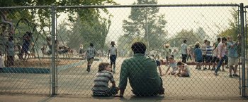 Movie still from “Timmy Failure: Mistakes Were Made” (2020), directed by Tom McCarthy – Two men sitting on the ground in front of a chain link fence; Medium shot, Over the shoulder angle