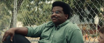 Movie still from “Timmy Failure: Mistakes Were Made” (2020), directed by Tom McCarthy – A man sitting in front of a chain link fence; Close Up shot, High angle