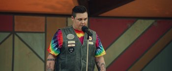 Movie still from “Timmy Failure: Mistakes Were Made” (2020), directed by Tom McCarthy – A person with tattoos is speaking into a microphone; Medium shot, Over the shoulder angle