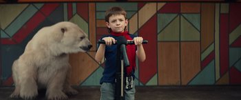 Movie still from “Timmy Failure: Mistakes Were Made” (2020), directed by Tom McCarthy – A boy in a blue shirt and a red scarf is on a scooter; Medium shot, Over the shoulder angle