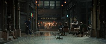 Movie still from “Tinker Tailor Soldier Spy” (2011), directed by Tomas Alfredson – A group of people sitting on a sidewalk in front of a building; Wide shot, High angle