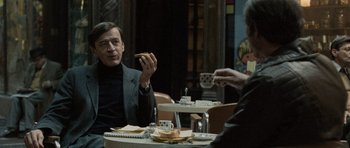 Movie still from “Tinker Tailor Soldier Spy” (2011), directed by Tomas Alfredson – A man sitting at a table eating a piece of pizza; Medium shot, Over the shoulder angle