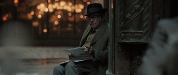 Movie still from “Tinker Tailor Soldier Spy” (2011), directed by Tomas Alfredson – An old man sitting on the side of the street reading a newspaper; Medium shot, Over the shoulder angle