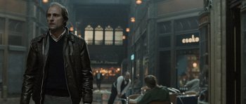 Movie still from “Tinker Tailor Soldier Spy” (2011), directed by Tomas Alfredson – A man in a leather jacket standing next to a building; Medium shot, Over the shoulder angle