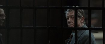 Movie still from “Tinker Tailor Soldier Spy” (2011), directed by Tomas Alfredson – An older man standing behind bars in front of a window; Close Up shot, Over the shoulder angle
