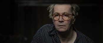 Movie still from “Tinker Tailor Soldier Spy” (2011), directed by Tomas Alfredson – An older man wearing glasses looking at the camera; Close Up shot, Over the shoulder angle