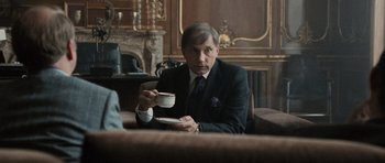 Movie still from “Tinker Tailor Soldier Spy” (2011), directed by Tomas Alfredson – A man sitting at a table holding a cup of coffee; Medium shot, Over the shoulder angle