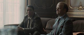 Movie still from “Tinker Tailor Soldier Spy” (2011), directed by Tomas Alfredson – Two men in suits sitting on a couch in front of a window; Medium shot, Over the shoulder angle