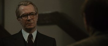 Movie still from “Tinker Tailor Soldier Spy” (2011), directed by Tomas Alfredson – A person wearing a suit and glasses; Close Up shot, Low angle