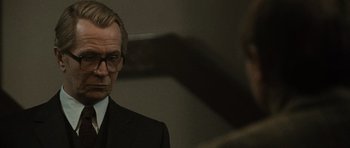 Movie still from “Tinker Tailor Soldier Spy” (2011), directed by Tomas Alfredson – A man wearing a suit and glasses in front of a mirror; Close Up shot, Over the shoulder angle
