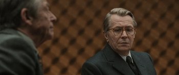 Movie still from “Tinker Tailor Soldier Spy” (2011), directed by Tomas Alfredson – A man in a suit and glasses looking at another man in a suit; Close Up shot, Over the shoulder angle